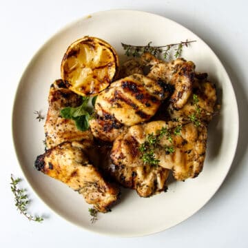 Grilled Boneless Chicken Thighs piled on a white plate garnished with thyme.