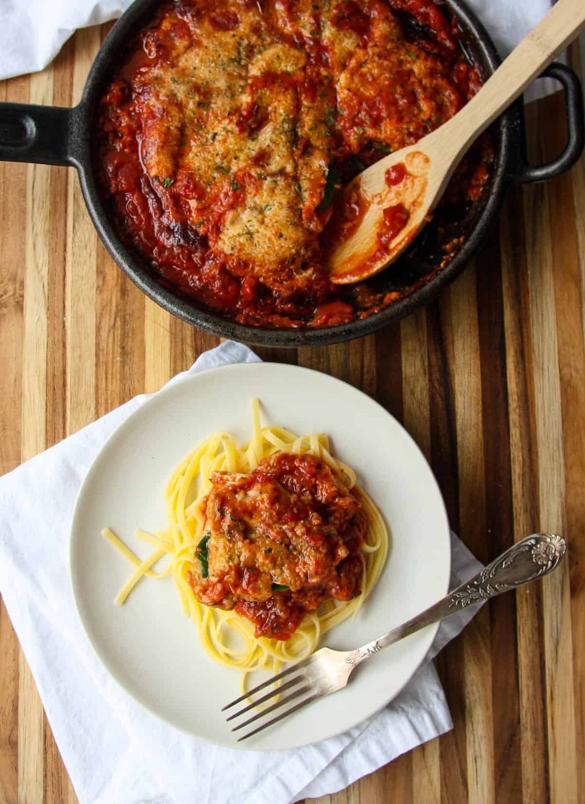 Chicken being served over pasta from a skillet.