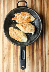 Three chicken breasts being seared in a cast iron skillet.