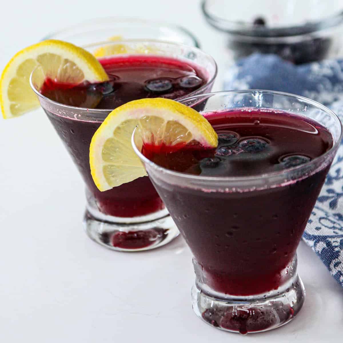 Two blueberry martinis with garnished with lemon slices and blueberries.