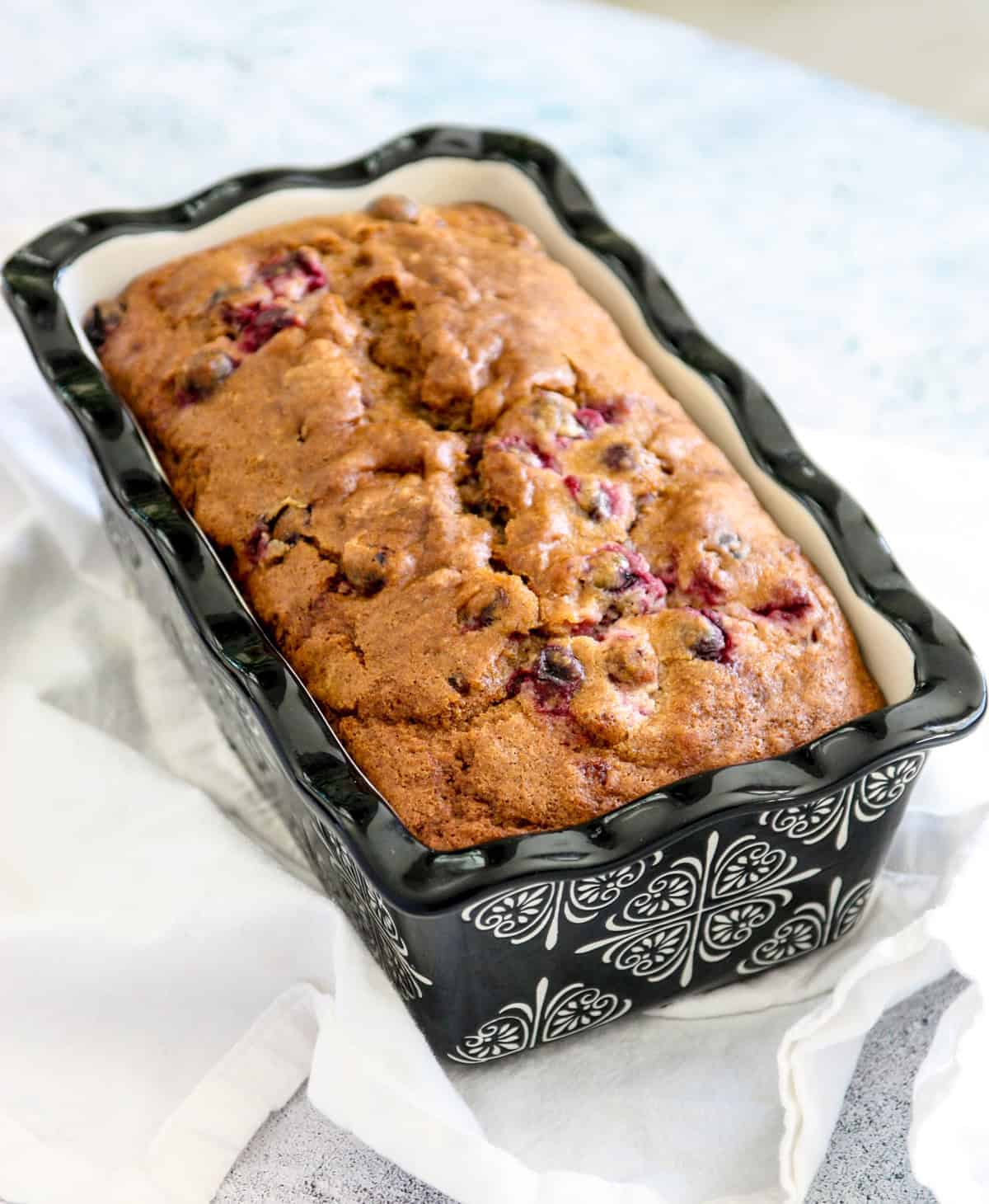 A loaf of cranberry walnut bread in a black and white ceramic pan.