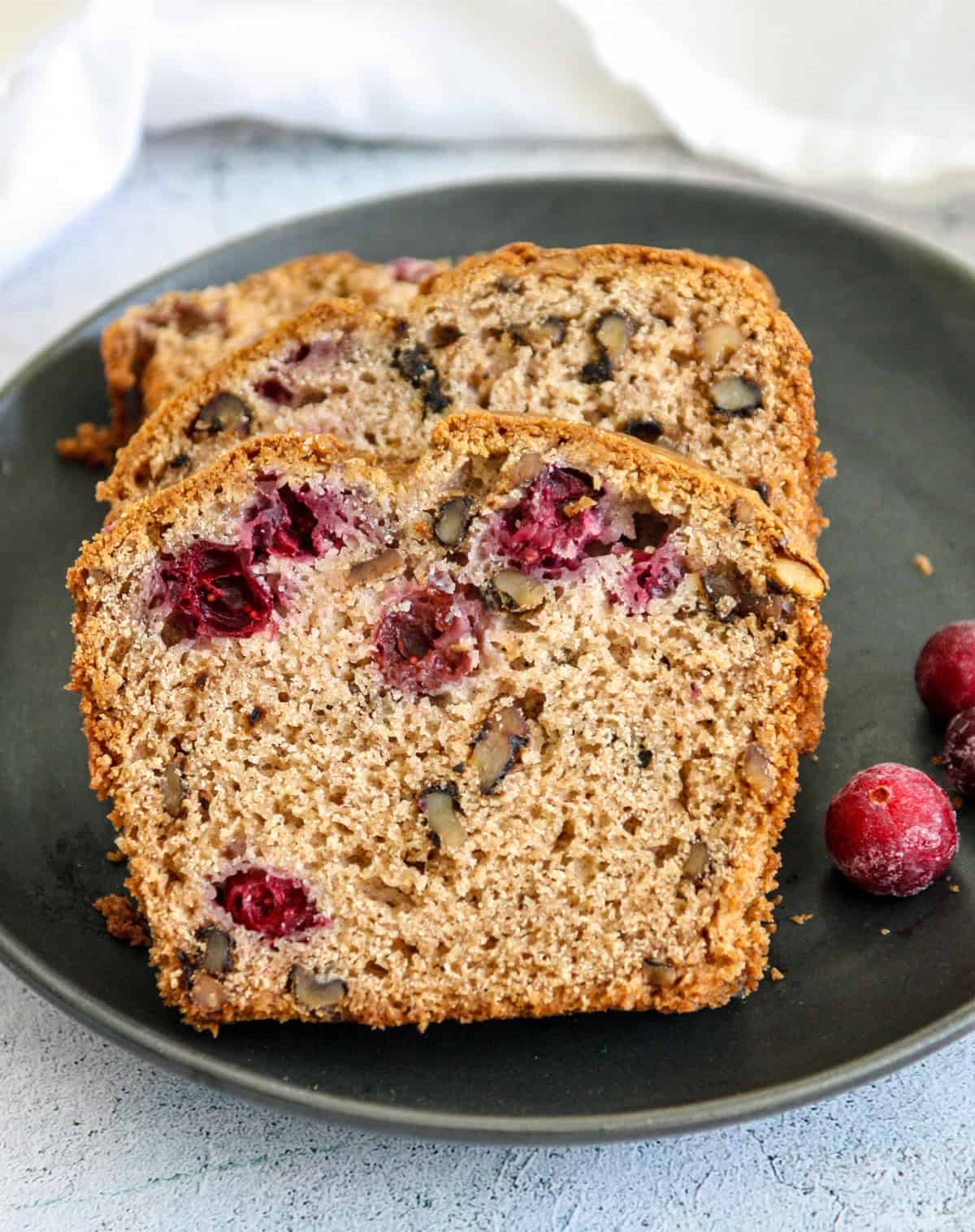 Three slices of cranberry walnut bread on a black plate.
