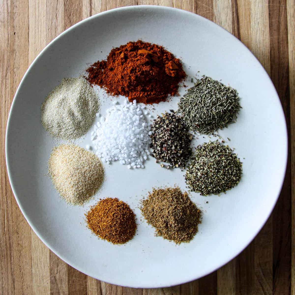 All of the spices for homemade Cajun seasoning in separate piles on a white plate.