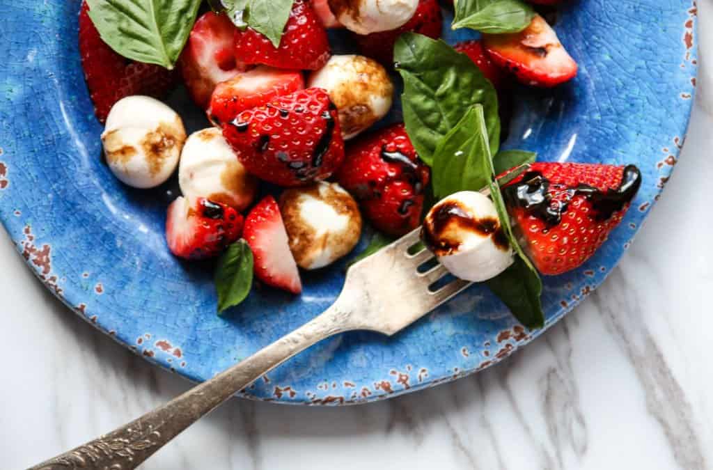 Top shot of basil, strawberries and mozzarella cheese balls on blue plate.