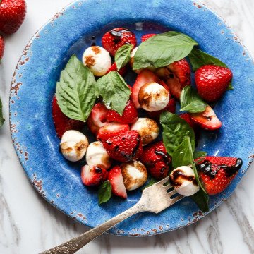 Strawberry caprese salad with fork on blue plate.