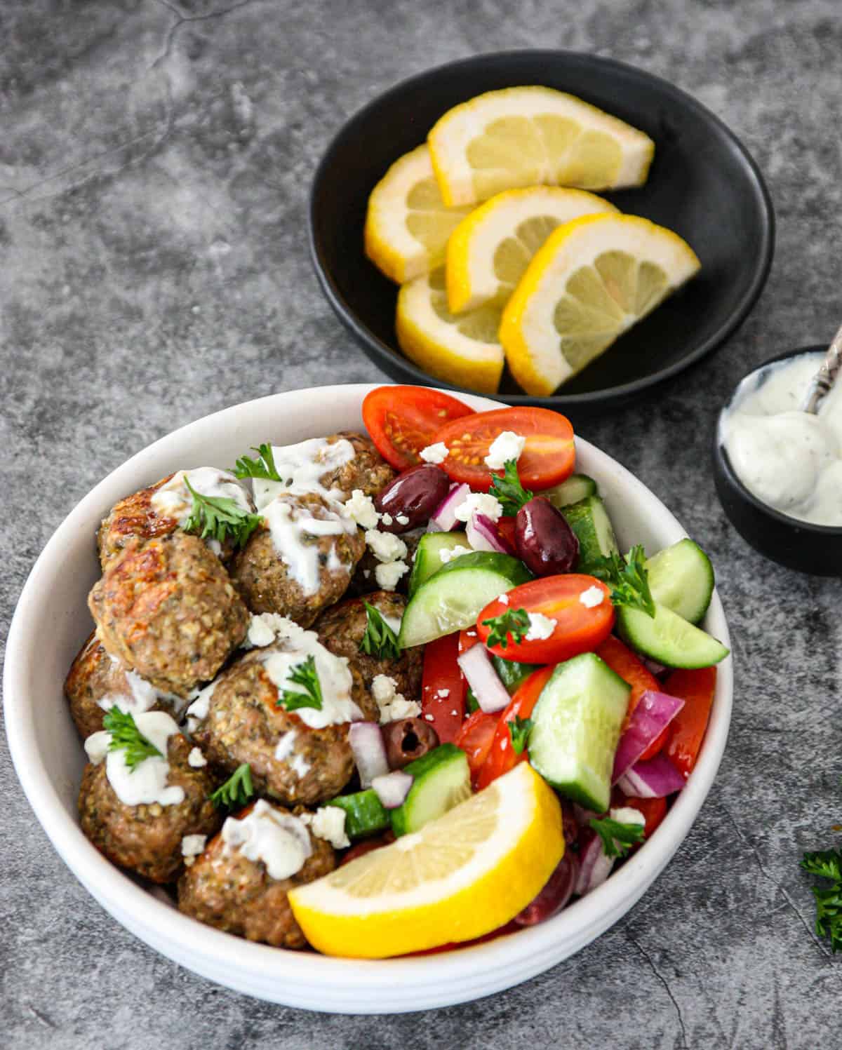 Greek chicken meatballs and Greek salad in a white bowl.