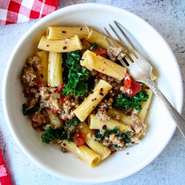 Sausage and kale pasta in a white bowl with a silver fork.