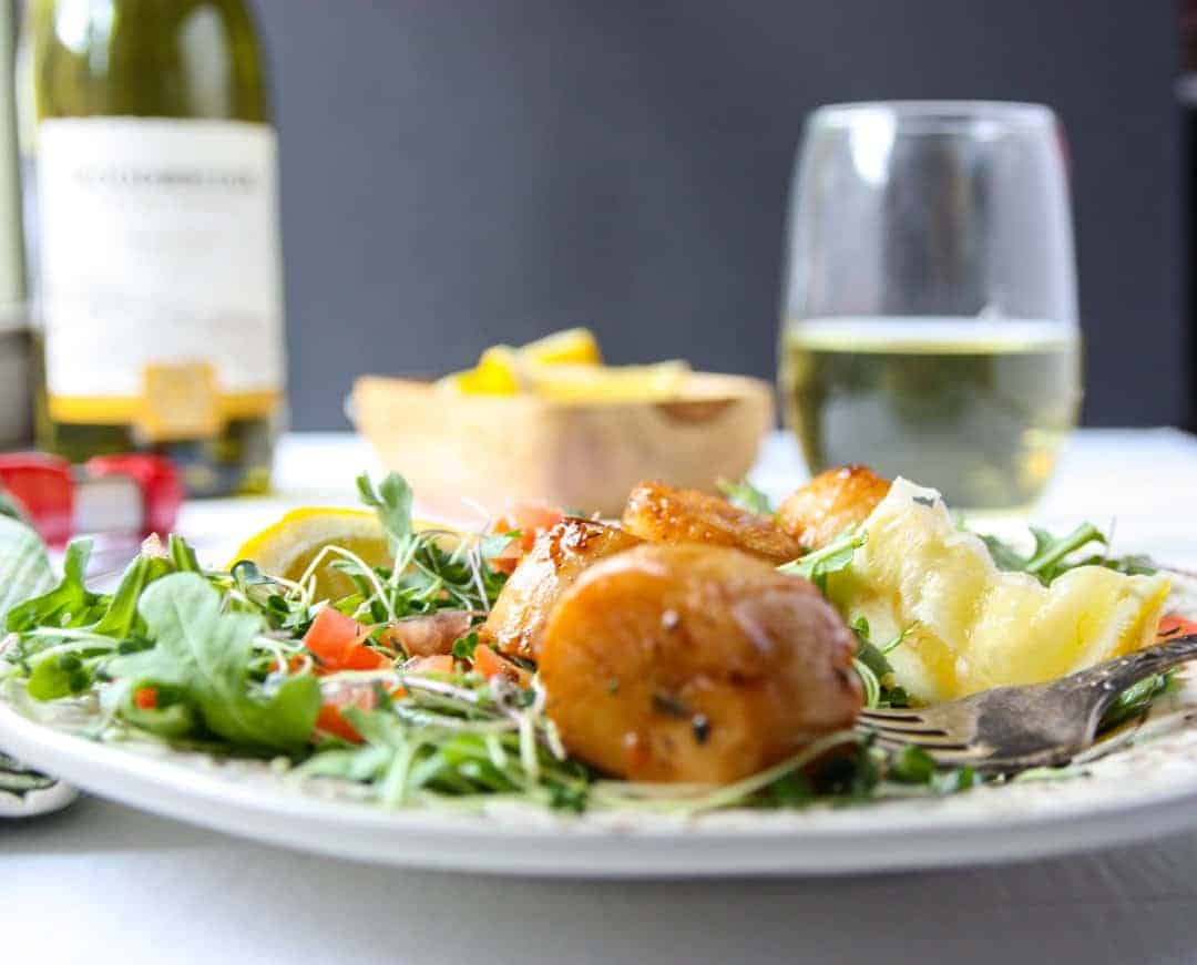 A close up of a plate of food on a table, with Scallops and Wine