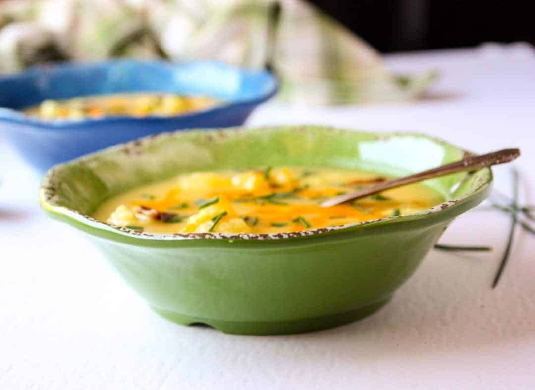 Two bowls of cheesy cauliflower soup in blue and green bowls