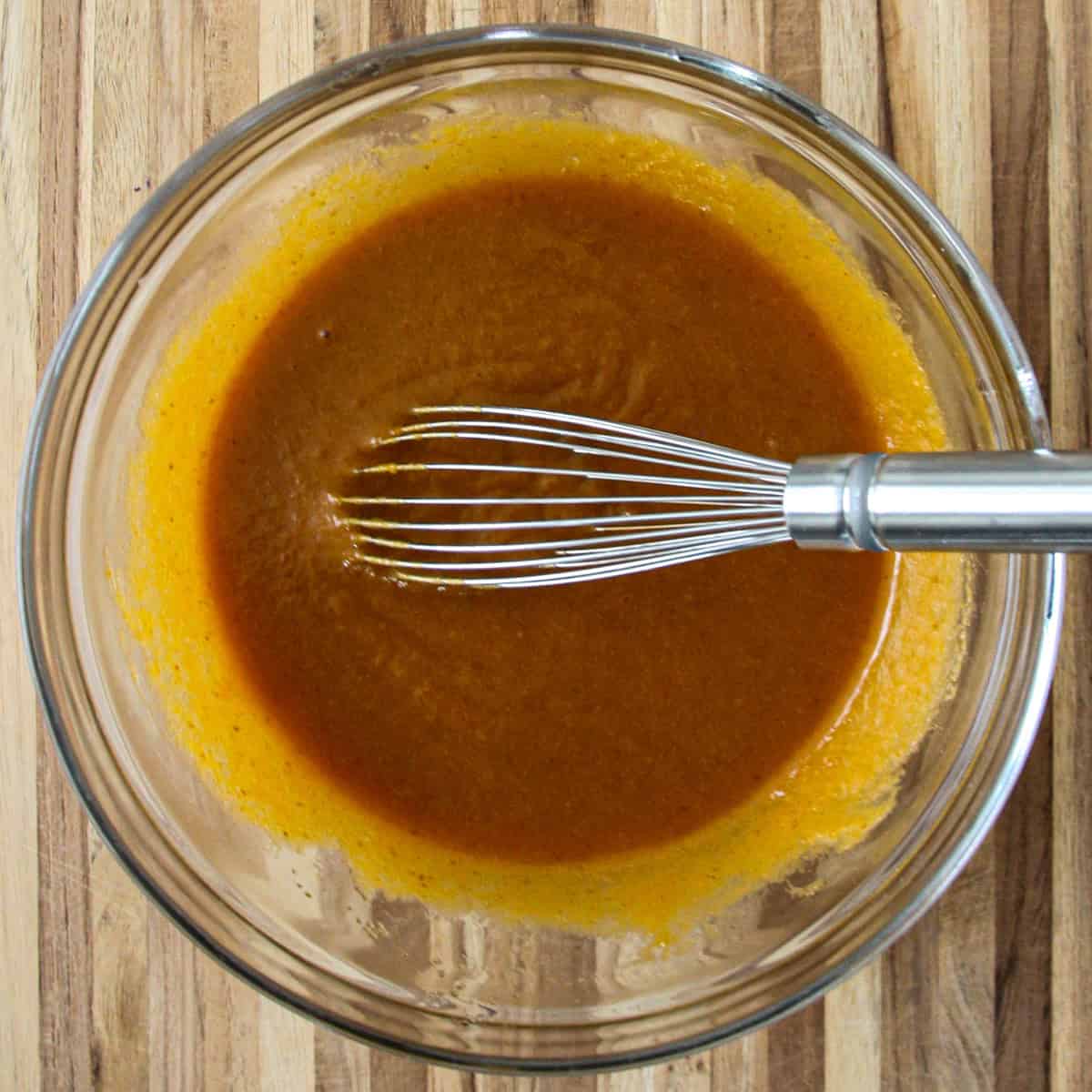 A mixture of oil, pumpkin puree, egg, sugar, and vanilla in a glass bowl with a whisk.