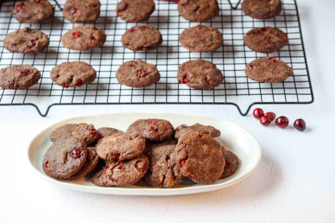 A white plate of chocolate cranberry cookies in front of cookies cooling on a wire rack