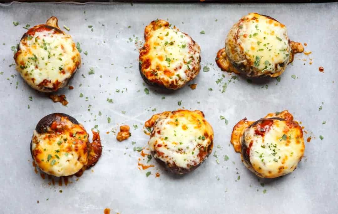 Six pizza stuffed mushrooms on a parchment lined baking sheet