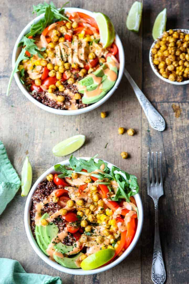 Two white bowls filled with Mexican seasoned grain and vegetables on a wooden table.