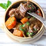 A bowl of Beef Stew with carrots and chunks of beef garnished with parsley.