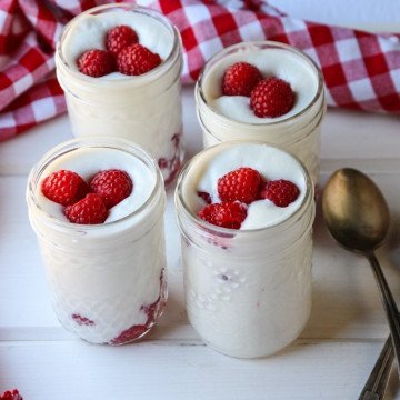 Four jars of mousse on a table, with raspberries