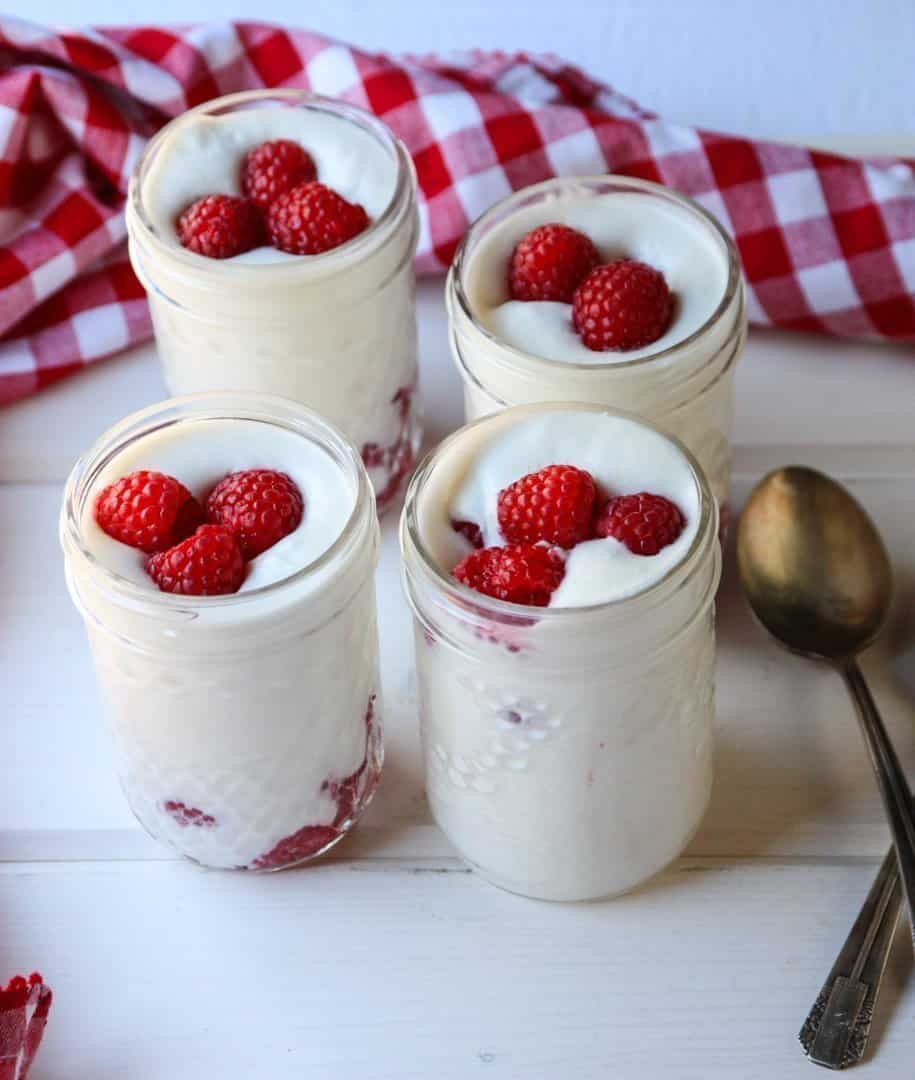 Four jars of mousse on a table, with raspberries