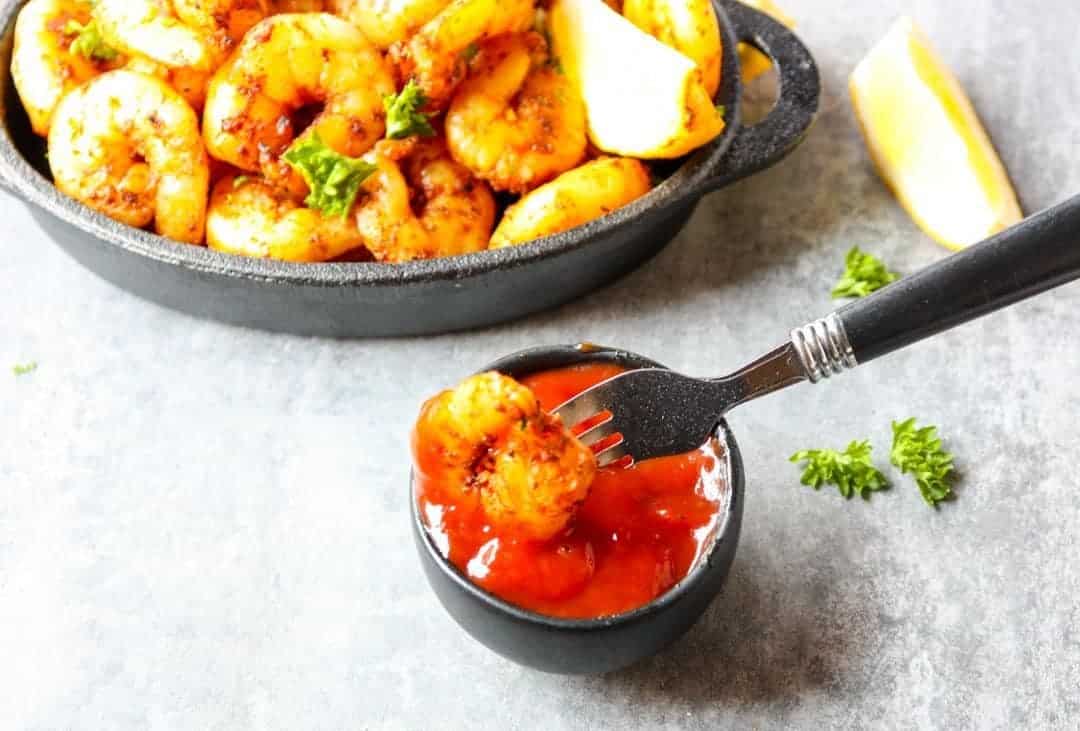A fork dipping a shrimp in cocktail sauce.