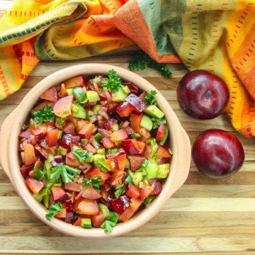 A bowl of fruit salsa on top of a wooden table, with Plums