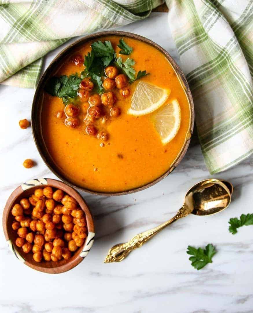 Bowl of sweet potato soup topped with lemon slices, roasted chickpeas, and parsley