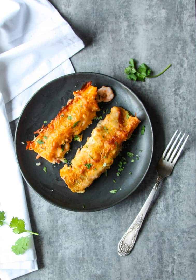Black plate with two seafood enchiladas and a white napkin & silver fork