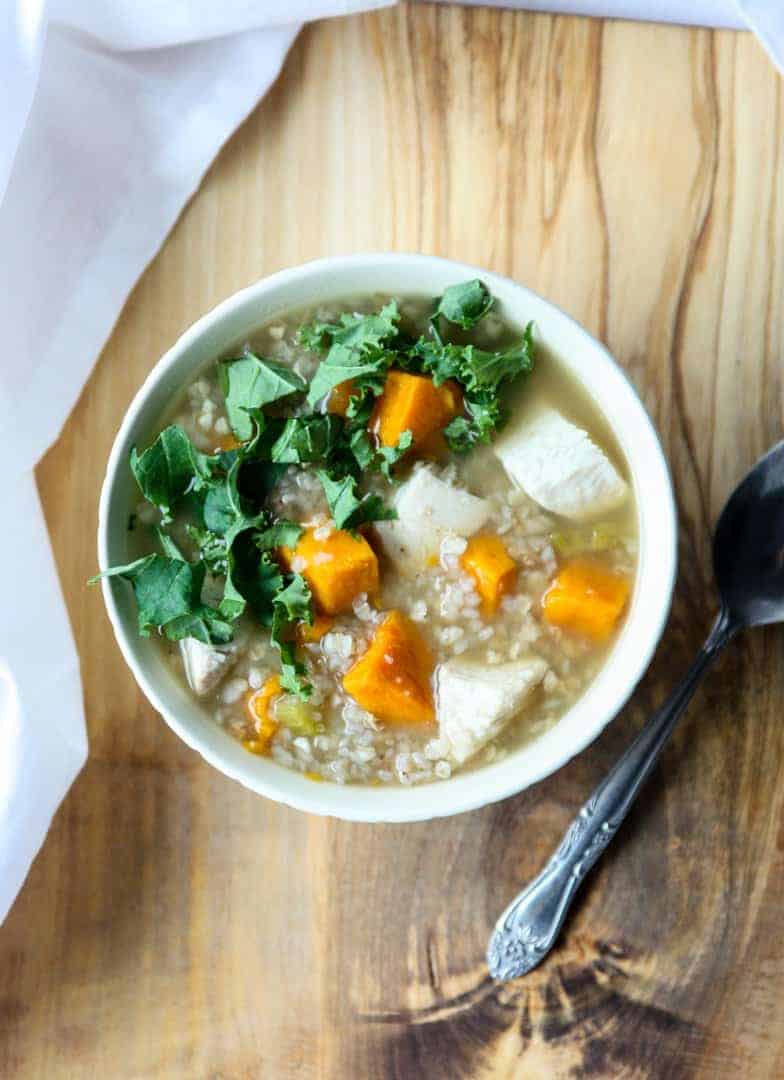 Buckwheat soup with turkey, sweet potato & kale in a white bowl on a wooden board