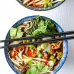 A bowl of vegetables and noodles with chopsticks