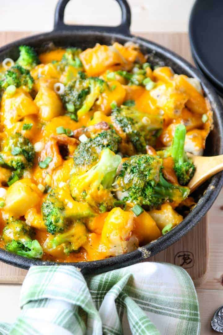 A close up of food with broccoli, chicken and potatoes in black skillet.
