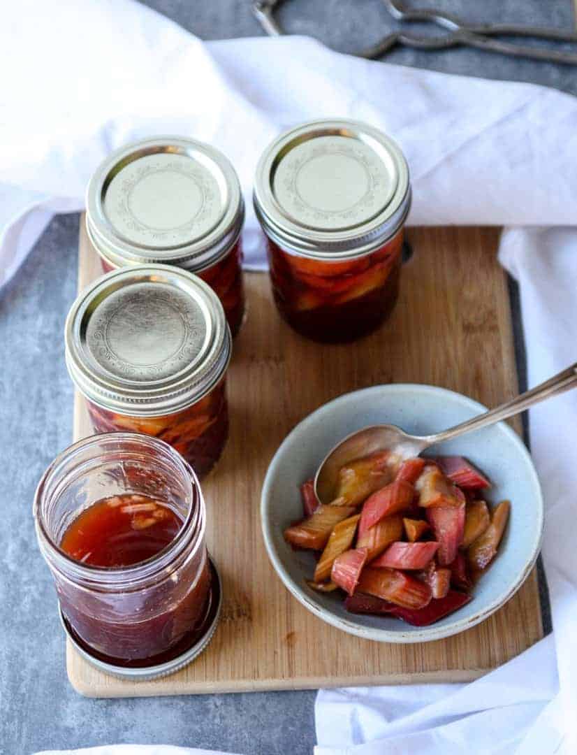 four jars of pickled rhubarb, on opened, and a dish of pickled rhubarb