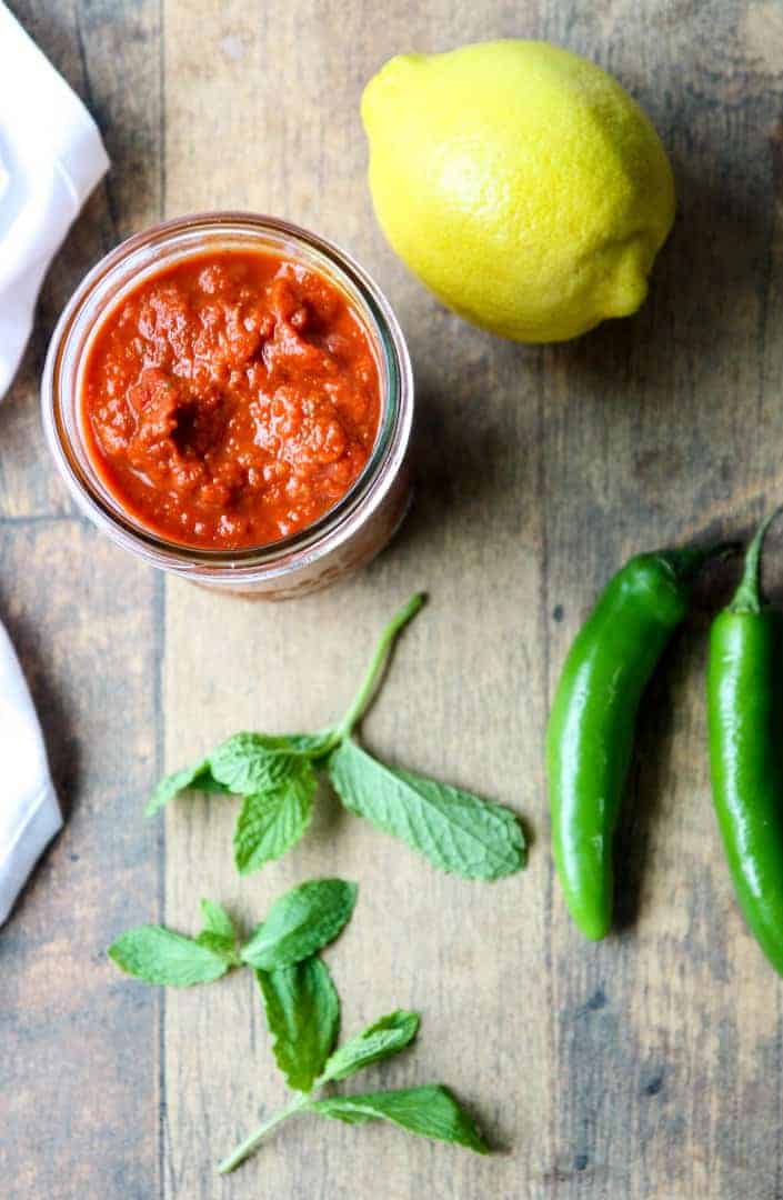 Jar of Harissa Paste with a lemon, two chile peppers and a sprig of mint.