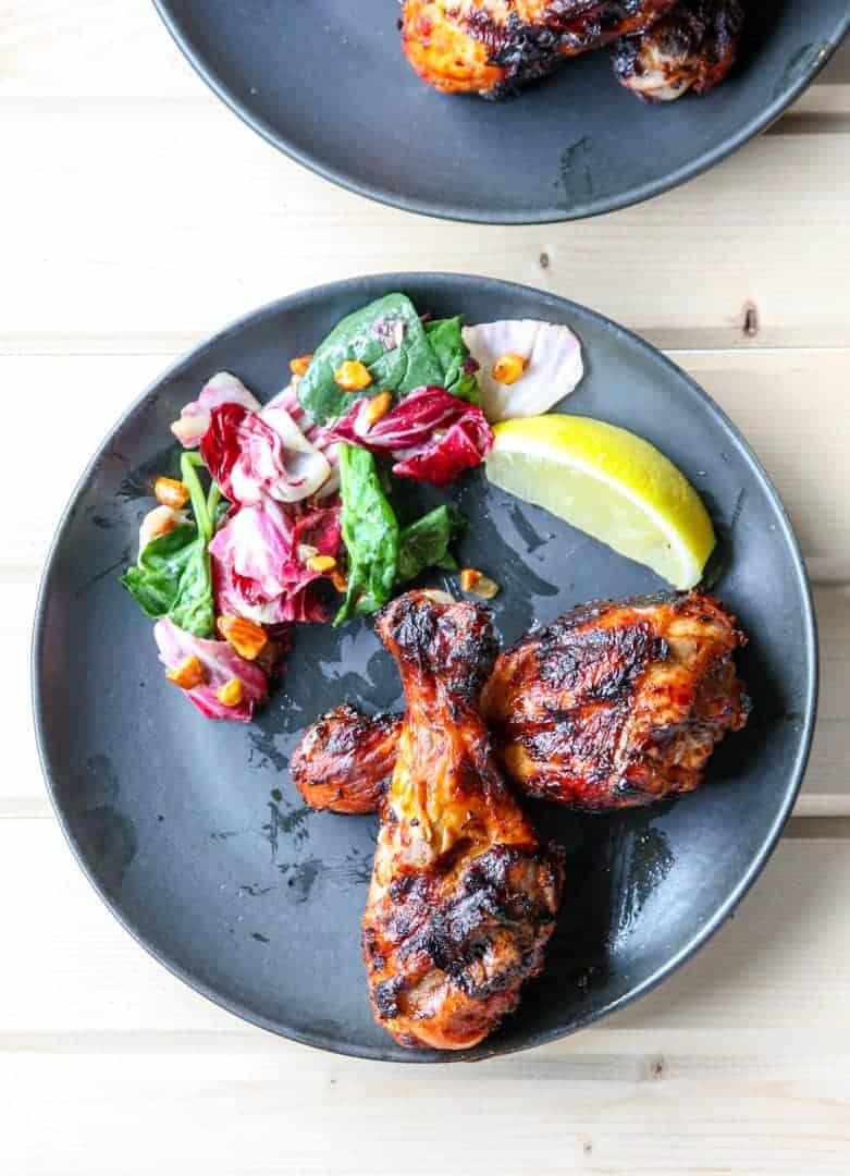Two grilled chicken drumsticks on a black plate with salad