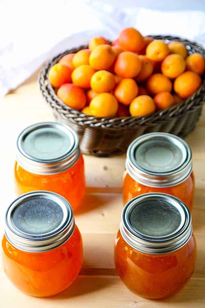 A basket of apricots and jars of jam on a table