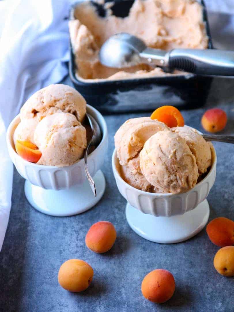 Two bowls of ice cream on a table with apricots and spoons