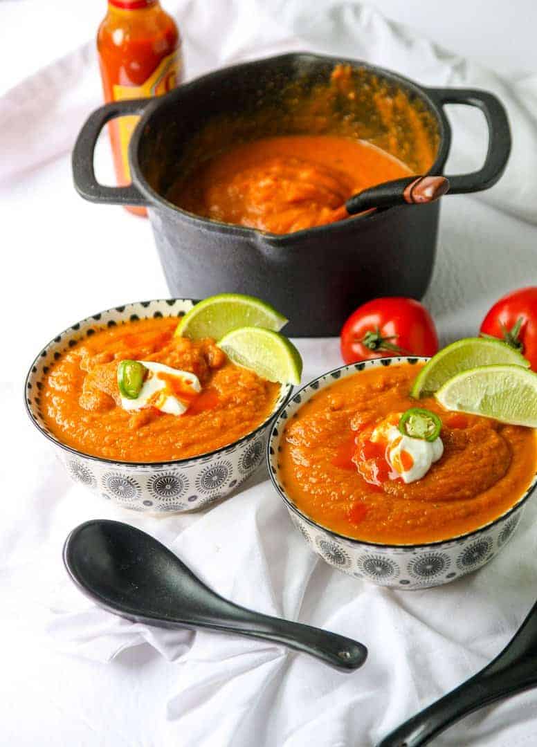 Two bowls of Southwestern Pumpkin Soup garnished with lime wedges and jalapeno slices