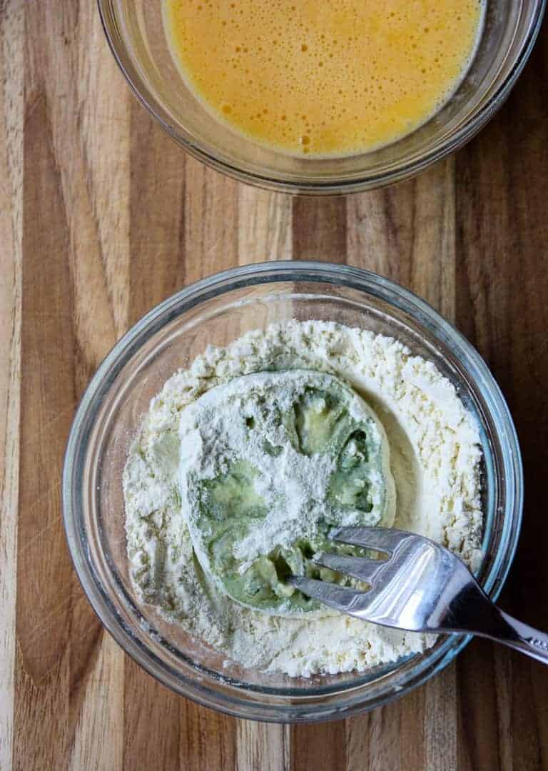 Green tomato slice being dredged in flour