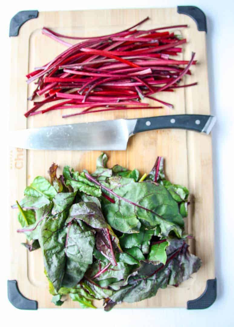 Beet leaves and stems on a wooden cutting board with a knife.