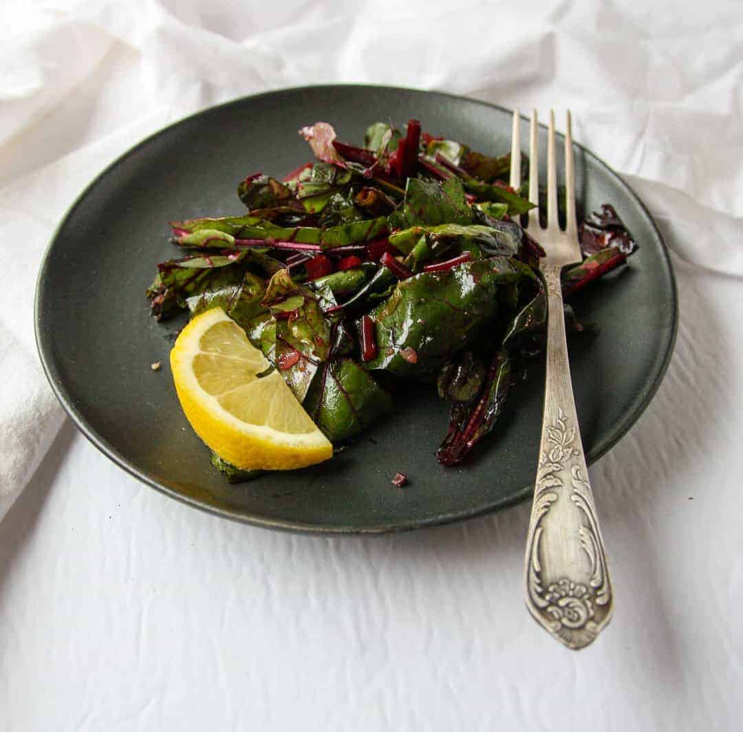 A plate of cooked greens and a lemon wedge on a table with a fork.
