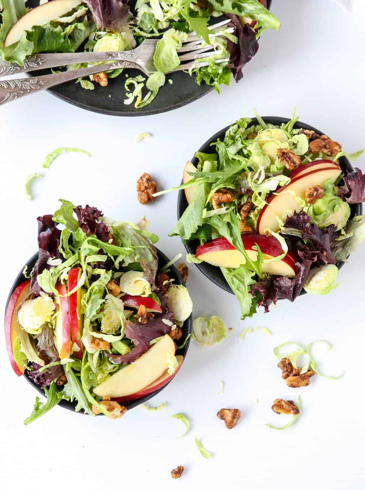 Salad on two black plates on a white table.