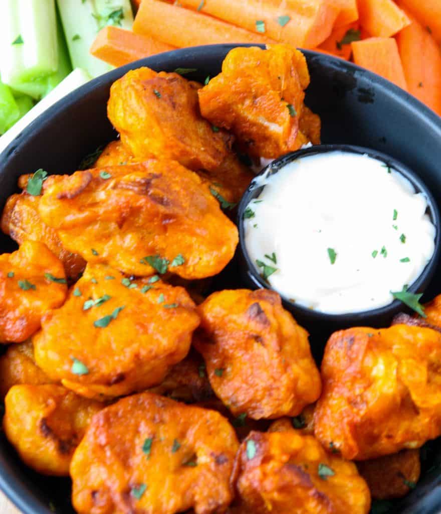 Close up of buffalo cauliflower bites on a black plate with a small dish of ranch dip.