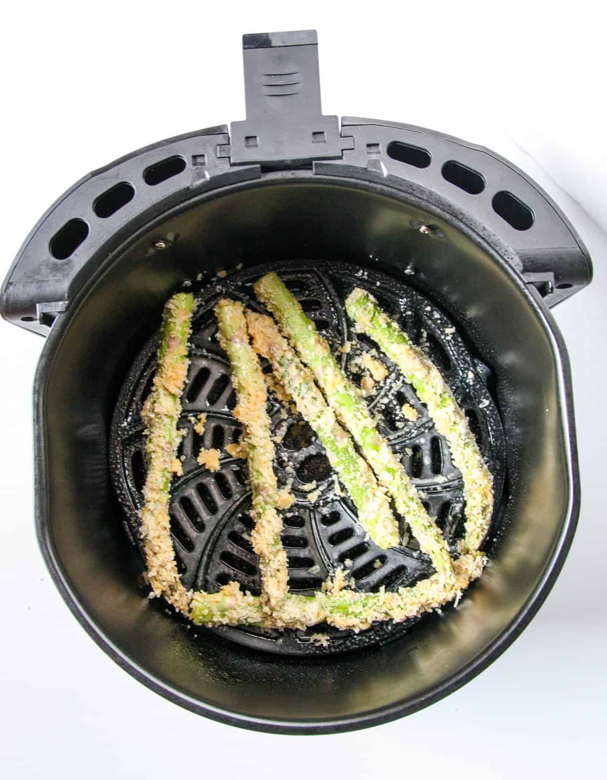 Coated asparagus spears in an air fryer basket ready to be cooked.