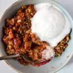 A bowl of rhubarb crisp topped with a scoop of vanilla ice cream.