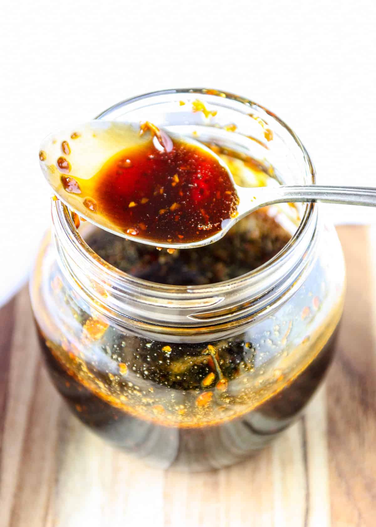 A spoon resting on top of a jar of honey teriyaki sauce.