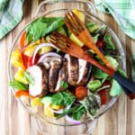 Salad in a glass bowl topped with sliced jerk chicken breast.