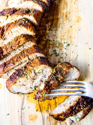 Sliced pork tenderloin on a wooden cutting board.