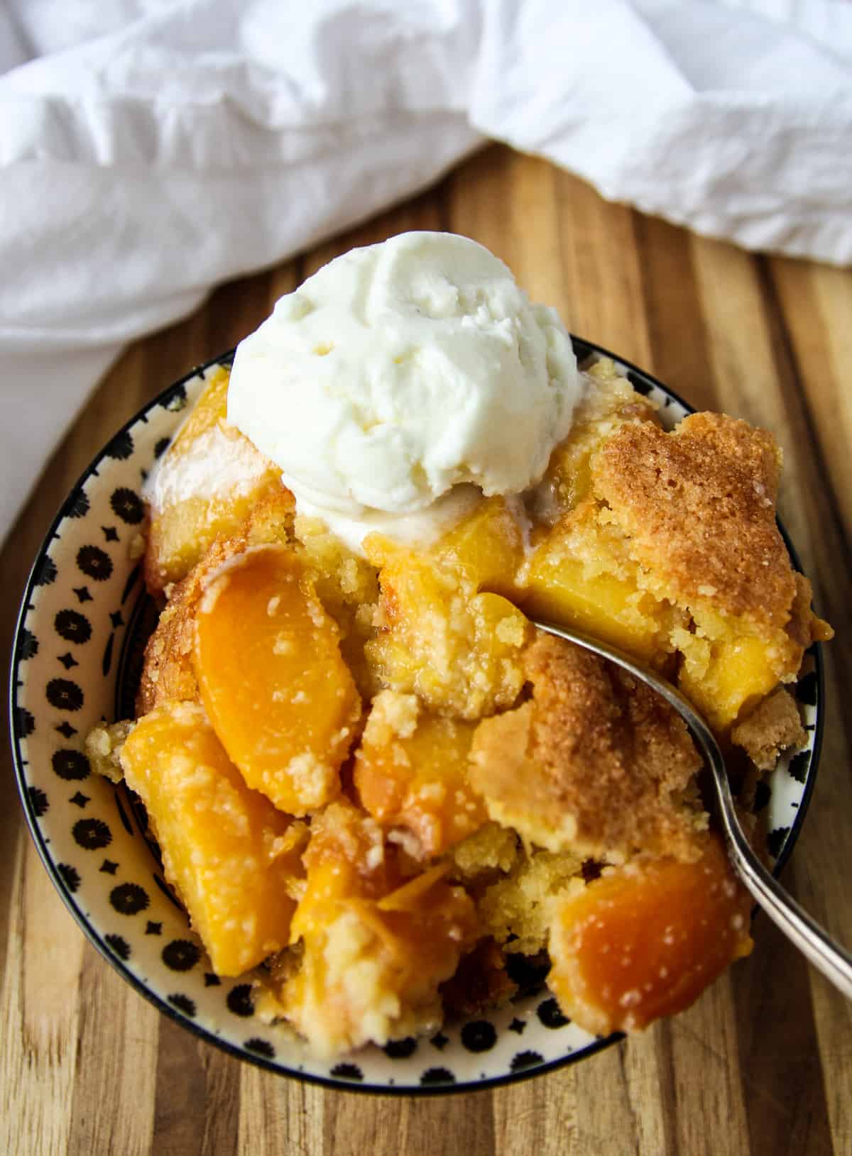 A bowl of gluten free peach cobbler with a spoon inserted.