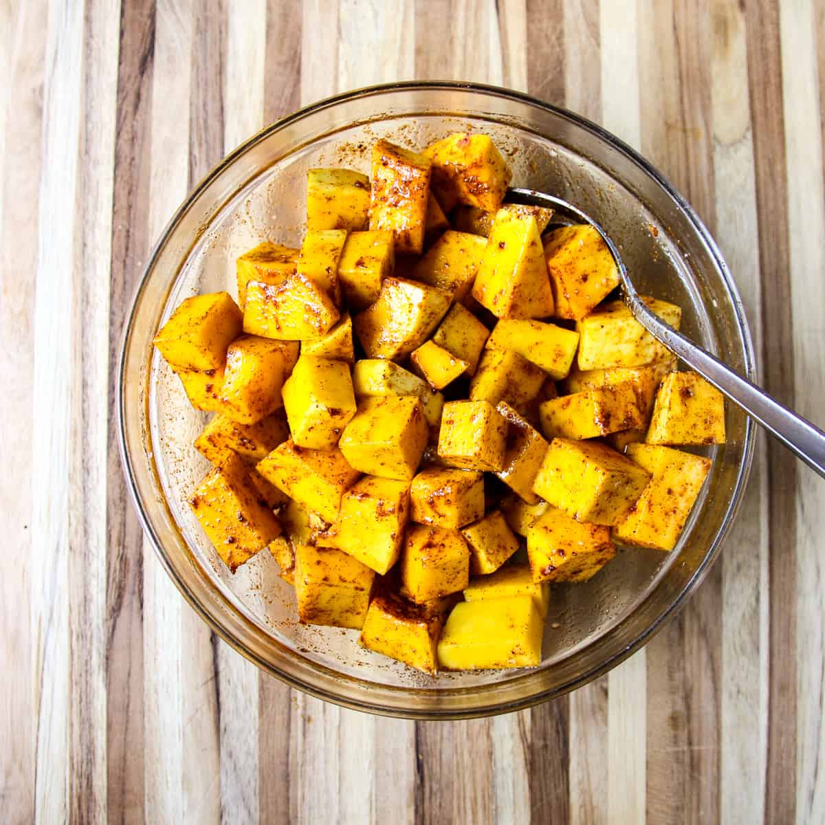 Butternut squash cubes being tossed in a bowl with seasonings and oil.