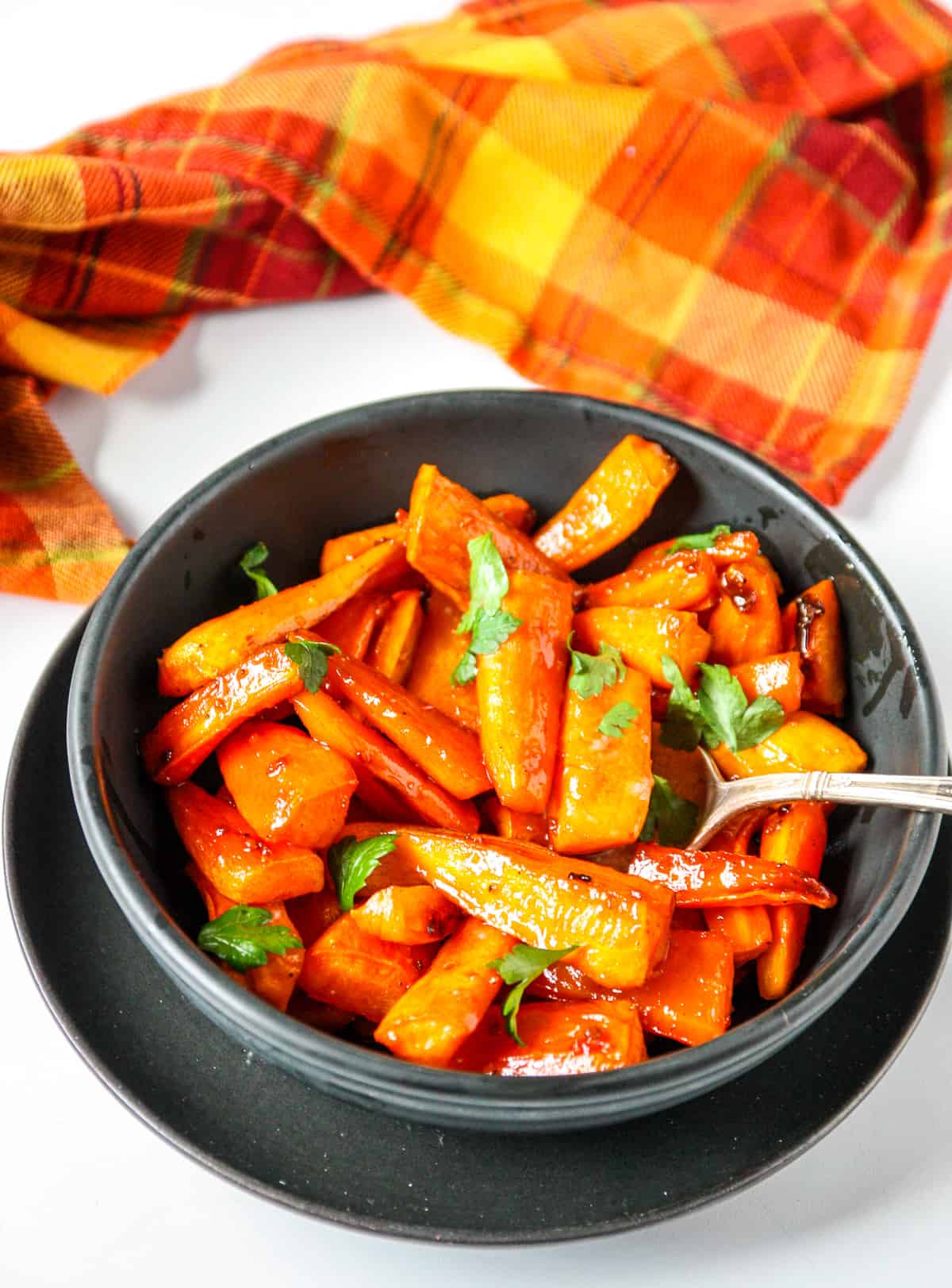 A bowl of brown sugar roasted carrots with a spoon inserted.