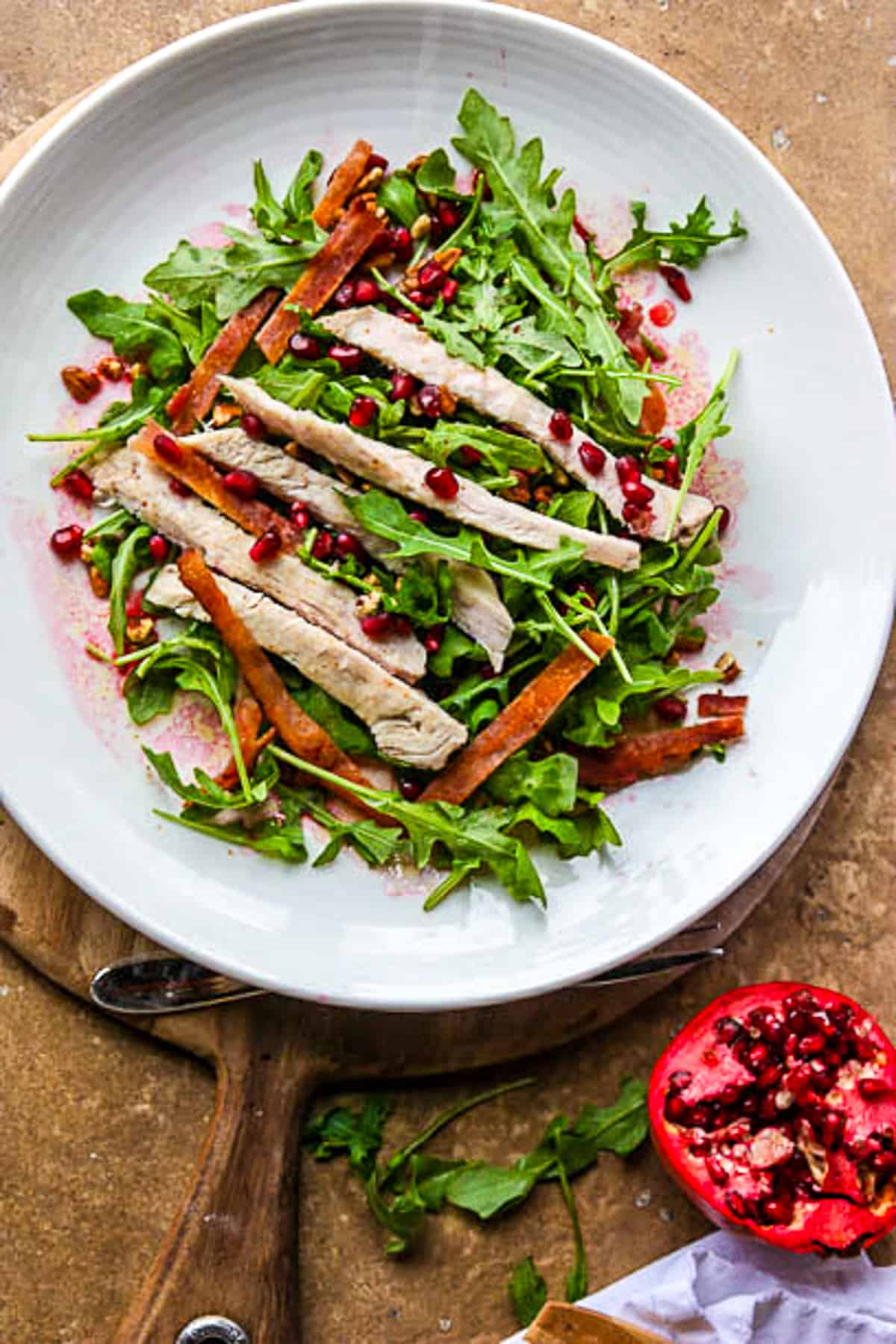 Club salad with turkey, arugula, and bacon on a white plate.