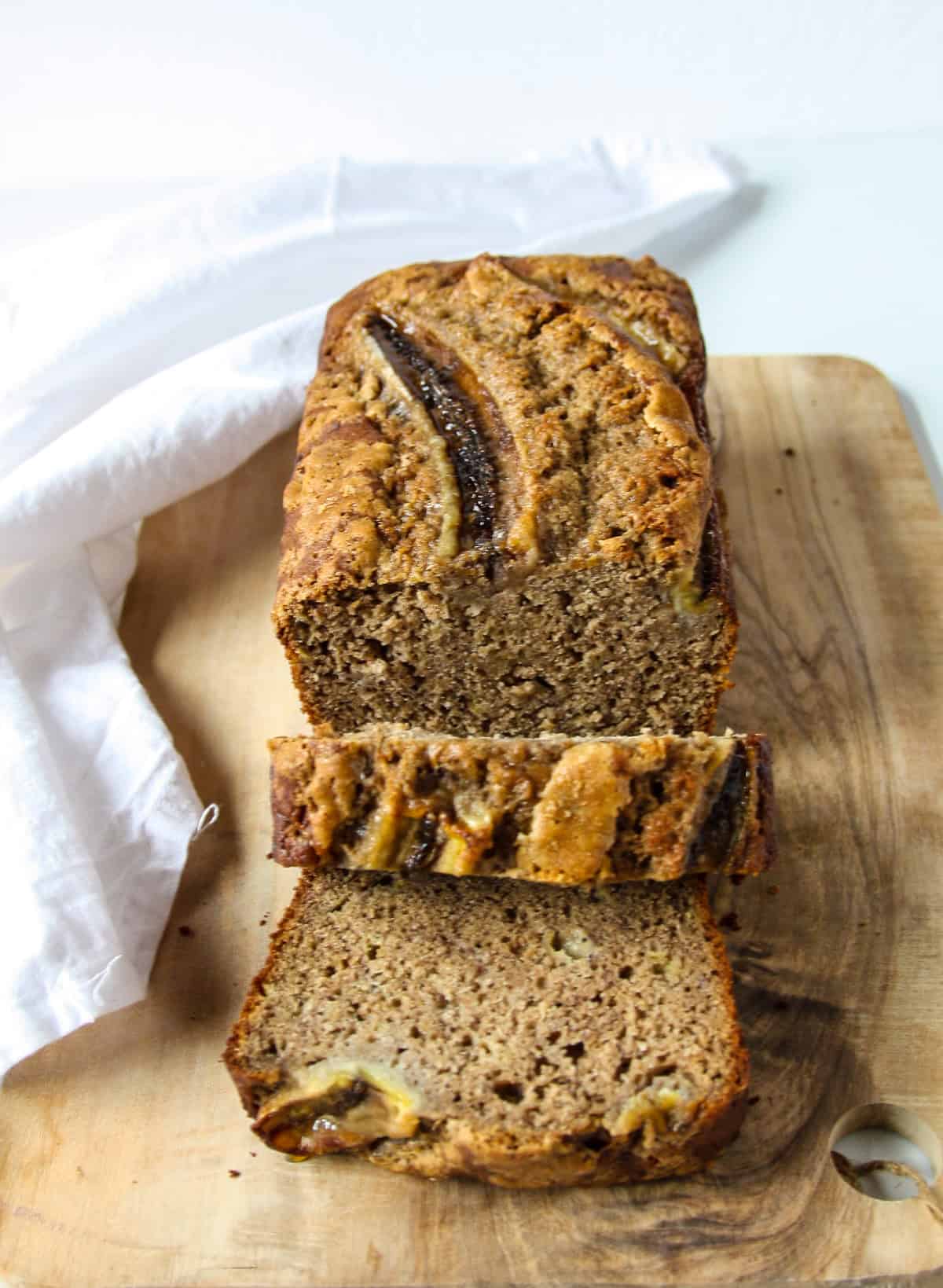 Partially sliced banana bread on a wooden cutting board.