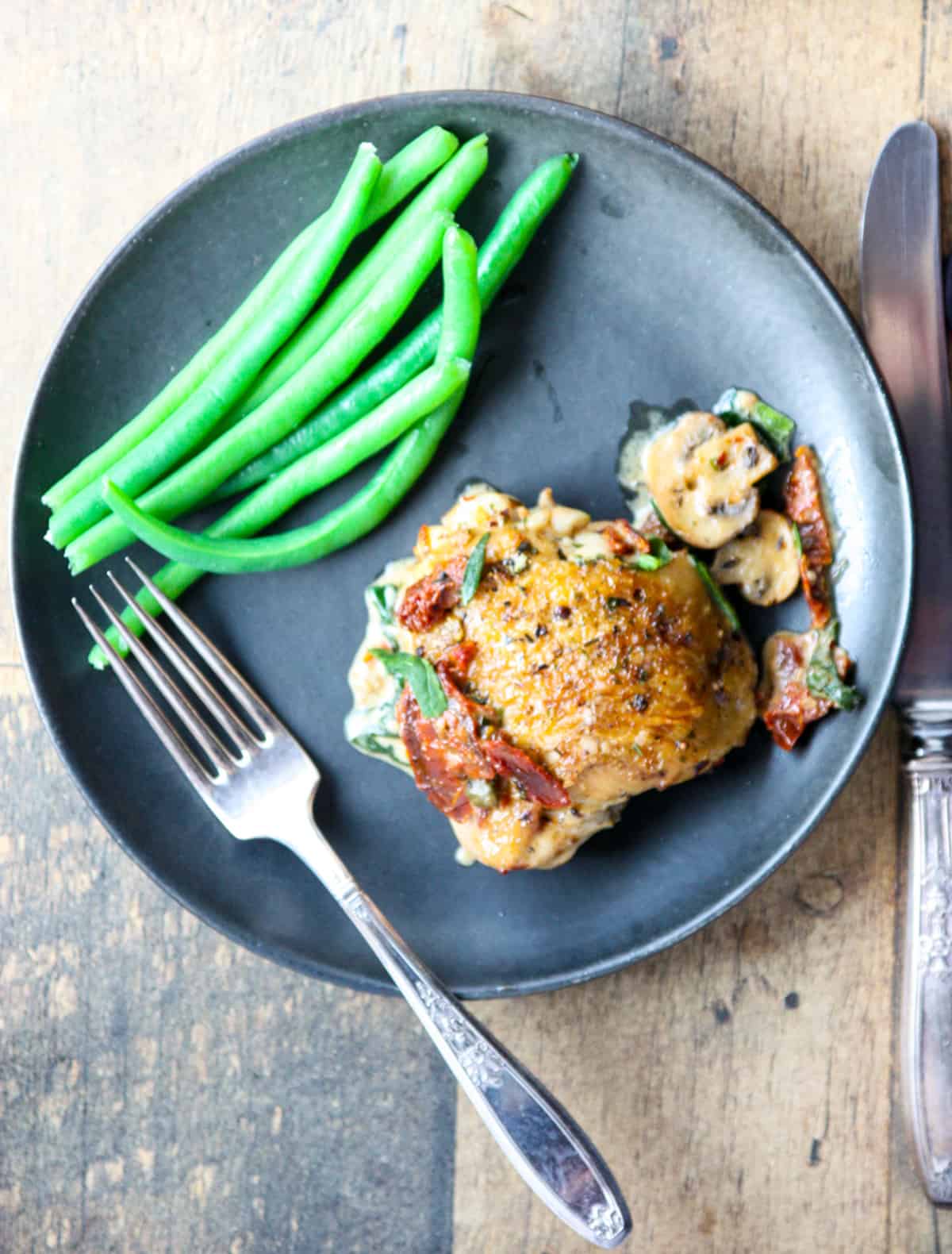 A piece of chicken on a black plate with green beans.