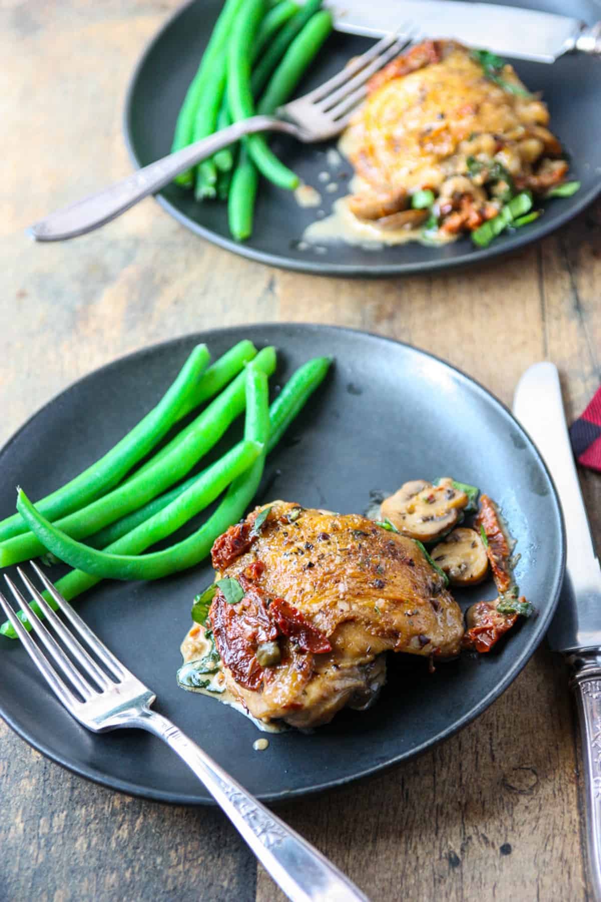 A piece of marry me chicken on a black plate with green beans